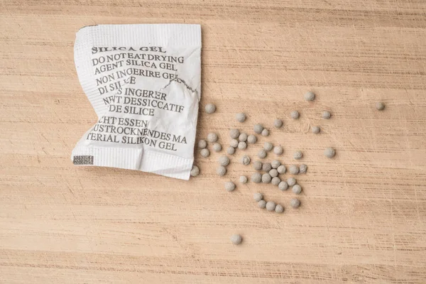 Desiccant or silica gel in white paper packaging, spread on the wooden background