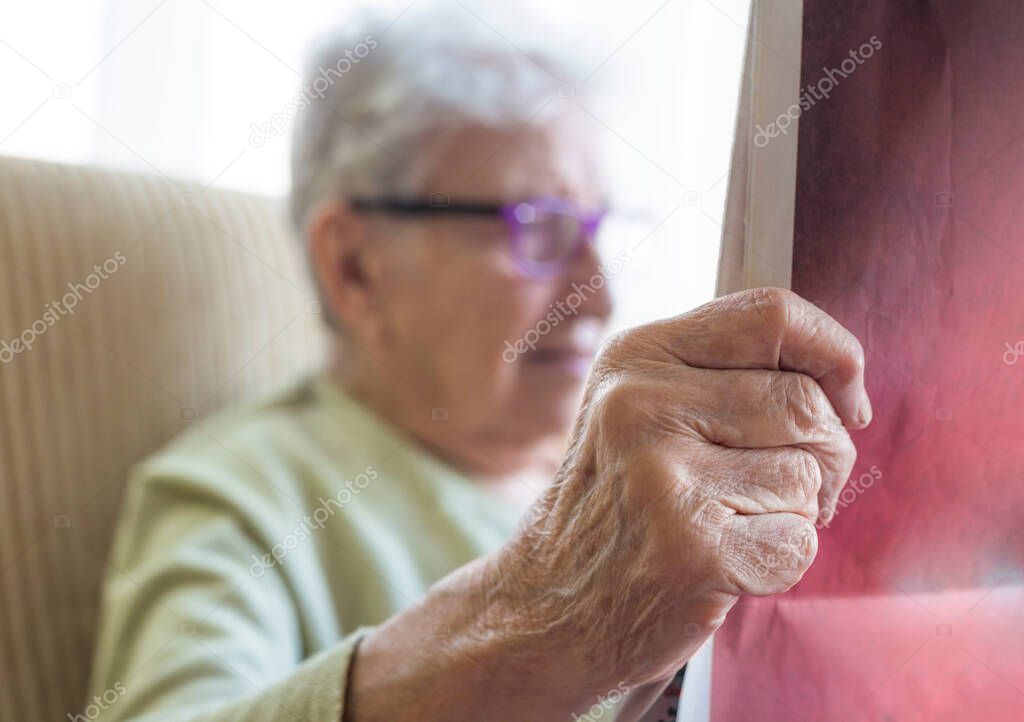 closeup wrinkled hand of a senior person reading newspaper at home
