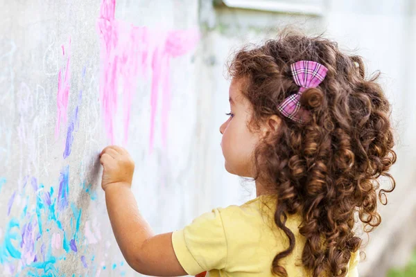 Кудрявая Милая Девочка Рисует Мелом Стене — стоковое фото
