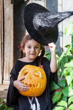 Cadılar Bayramı ve kutlama kavramı. Güzel çocuk kız cadı kostüm Cadılar Bayramı Balkabağı açık havada tutar