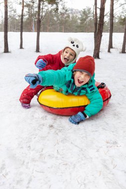 Boy and girl sliding down the hill on tubing sleds outdoors, winter day, ride down the hills, winter games and fun clipart