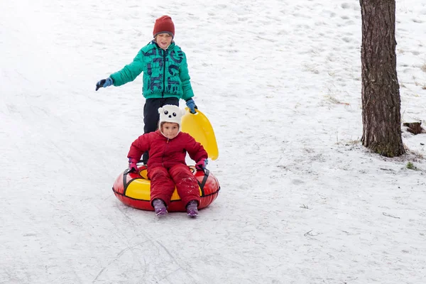 男の子と女の子のチューブそり 屋外の丘の上を滑る丘 冬のゲームおよび楽しみを下ると冬の日 — ストック写真