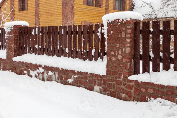 Wooden fence with a stone foundation covered with snow after a heavy snowfall in winter