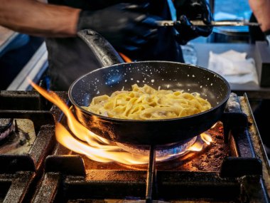 Şef tavada erişte ve sebze pişiriyor, kremalı makarna kızartılmış tava ve alevler içinde. Sokak yemeği.
