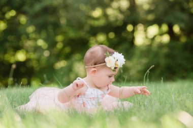 Sevimli bir yaşında beyaz kız dışında bir pembe yazlık elbise ve çiçek kafa bandı çim