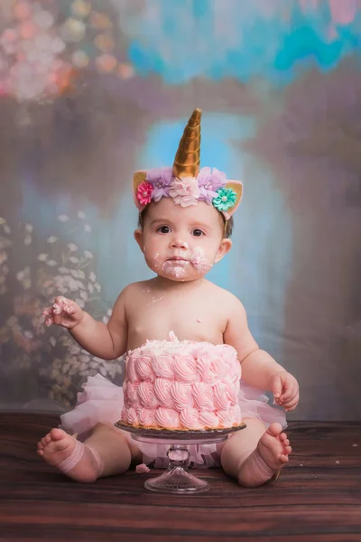 一岁的白种女孩穿着独角兽喇叭头戴头巾坐在粉红色 Smashcake 的前面 有很多的霜和糖衣 — 图库照片