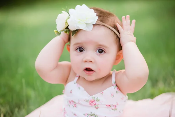 可爱的一岁白人女孩在草地上穿着粉红色的夏季礼服和花头带 — 图库照片