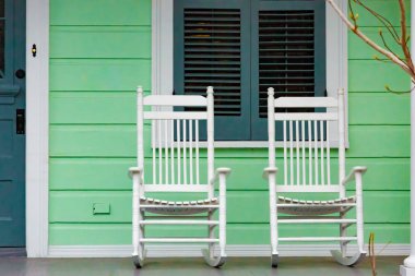 Yeşil New Orleans tarzı Amerikan evinin verandasında iki beyaz sallanan sandalye.