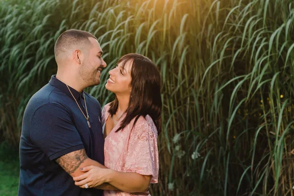 A happy young and in love engaged couple having an intimate moment outside. Kissing by farm field at sunset in summer.