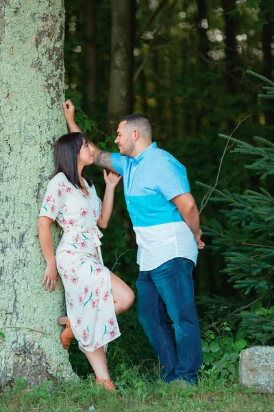 A young engaged couple enjoy a private moment in love with each other outside by tree