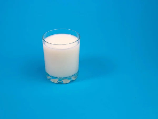 Glass of milk in transparent glass on blue background