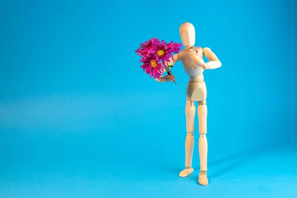 Wooden mannequin holding bouquet of flowers on blue background
