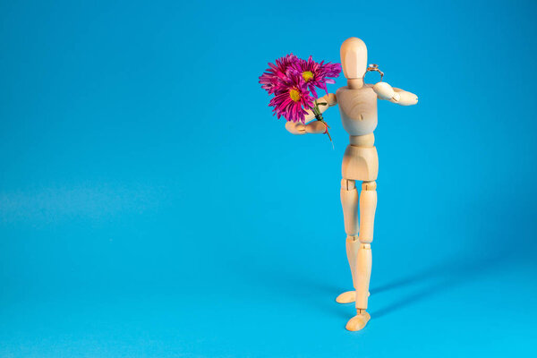 Wooden mannequin holding bouquet of flowers on blue background