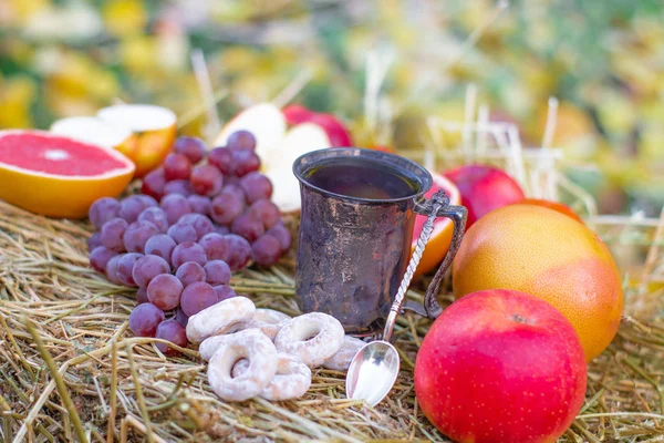 Delicious ripe fruits and cup of tea on haystack, close up view