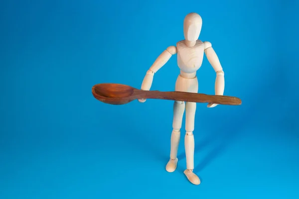 Wooden mannequin with wooden spoon on blue background