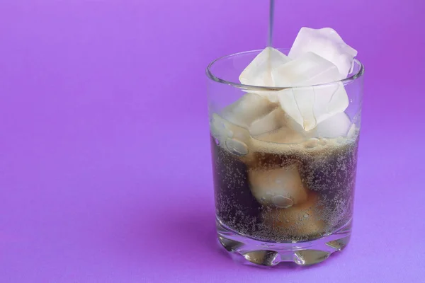 black carbonated drink with ice in a glass