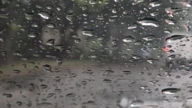 Yağmur damlalarıyla kaplı bir arabanın yan aynasına yakın çekim, ıslak bir yolu ve farları açık beyaz bir aracı yansıtıyor. Bulanık arkaplan ve su damlacıkları yağmurlu hava ve sürüş koşullarını anımsatıyor.