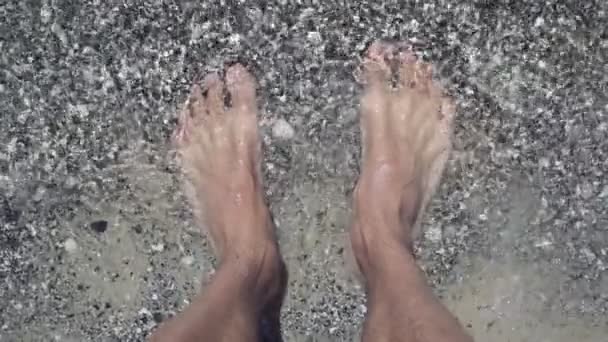 Pés masculinos na praia à beira-mar, vista para cima. Homem em pé na praia com água cobrindo os pés. Verão e relaxar conceitos. Movimento lento — Vídeo de Stock