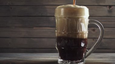 Soğuk karanlık bira bira bardağı dökme. Koyu ahşap arka plan üzerinde. Ağır çekim