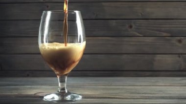 Soğuk karanlık bira bir cam içine dökme. Koyu ahşap arka plan üzerinde. Ağır çekim