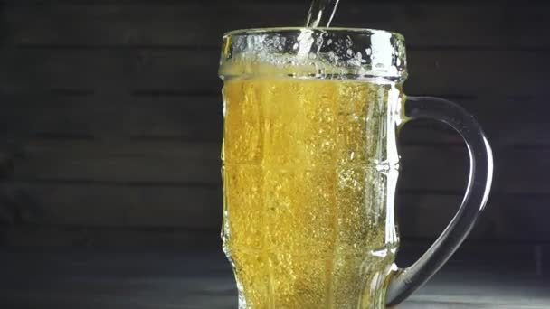 Lento tiro em movimento de derramar cerveja em caneca de cerveja. Sobre fundo de madeira escura — Vídeo de Stock