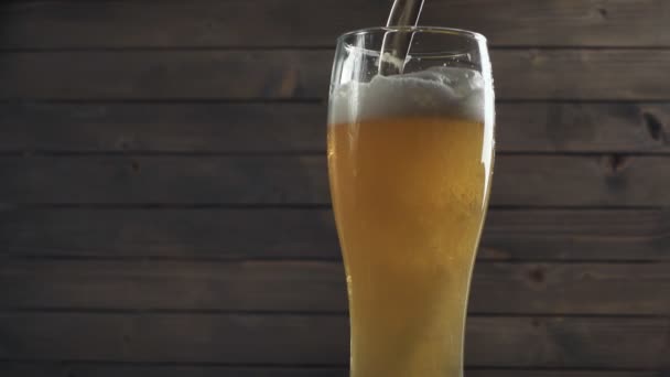 Пиво налито в стекло на деревянном фоне. Пена скользит вниз. Медленное движение — стоковое видео