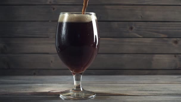把冰冷的黑啤酒倒入玻璃杯中。在黑暗的木质背景。慢动作 — 图库视频影像