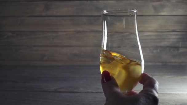 Hand som håller i ett glas whisky. Kvinnan skakar alkohol i baren. — Stockvideo