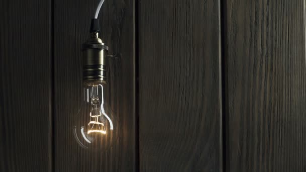 Light bulb illuminates on wooden background — Stock Video