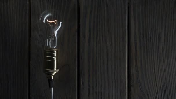 Light bulb illuminates on wooden background — Stock Video