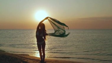 İnce genç kadın gün batımında sahilde dans ediyor.