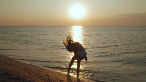 Slim young woman is dancing on the beach at sunset. — Stock Video