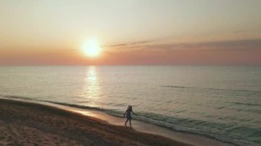 Gün batımında okyanus sahilinde yürüyen bir kadının güzel sahnesi. Joyful mutlu kız kilo kaybı diyet kavramı için ince vücutta sevinç ve mutluluk gösteren rahatlatıcı. Havadan görünüm.