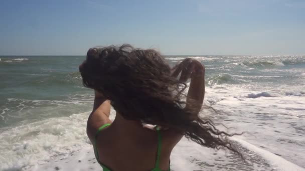 Μια γυναίκα αναπτύσσει τρίχες στον άνεμο στο φόντο της θάλασσας. Πίσω όψη. Αργή κίνηση. — Αρχείο Βίντεο