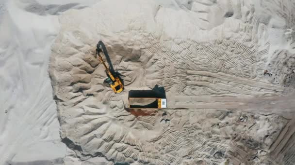 Aerial view of bulldozer loading sand into empty dump truck in open air quarry. — Stock Video