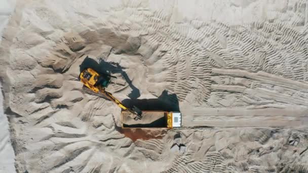 Aerial view of bulldozer loading sand into empty dump truck in open air quarry. — Stock Video