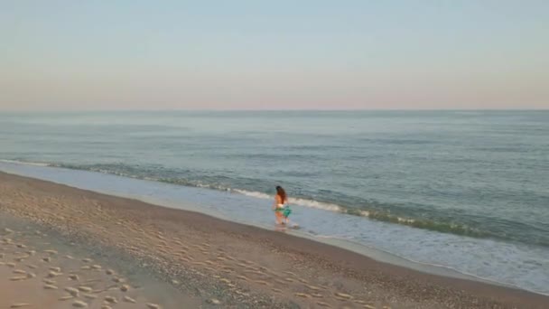 Όμορφη σκηνή μιας γυναίκας που περπατάει στην παραλία του ωκεανού το ηλιοβασίλεμα. Χαρούμενο ευτυχισμένο κορίτσι χαλάρωσης δείχνοντας χαρά και ευτυχία σε λεπτό σώμα για δίαιτα απώλειας βάρους έννοια. Αεροφωτογραφία. — Αρχείο Βίντεο