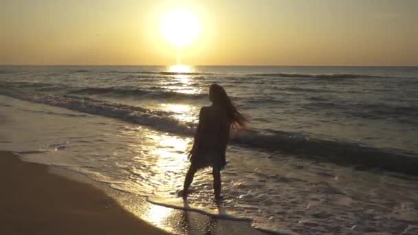 Schlanke junge Frau tanzt bei Sonnenuntergang am Strand. — Stockvideo