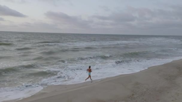 Štíhlá sportovní žena je na pobřeží sama, brzy ráno. Východ slunce — Stock video