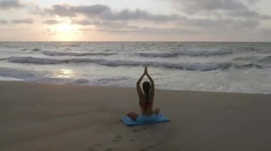 Fırtınalı denizin yakınında yoga egzersizleri yapan bir kız. Ağır çekim. Gün doğumu arkaplanı