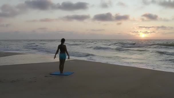 Fille faisant des exercices de yoga près de la mer orageuse. Au ralenti. Fond levant — Video