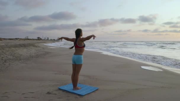 Chica haciendo ejercicios de yoga cerca del mar tormentoso. En cámara lenta. Fondo del amanecer — Vídeos de Stock