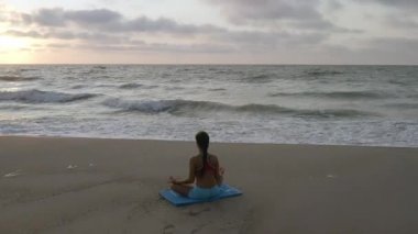 Fırtınalı denizin yakınında yoga egzersizleri yapan bir kız. Ağır çekim. Gün doğumu arkaplanı
