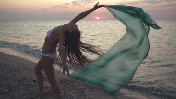 Schlanke junge Frau tanzt bei Sonnenuntergang am Strand. — Stockvideo
