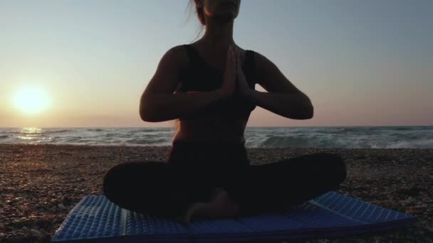 美丽的年轻女子一边坐在沙滩上一边看日落一边做瑜伽. — 图库视频影像