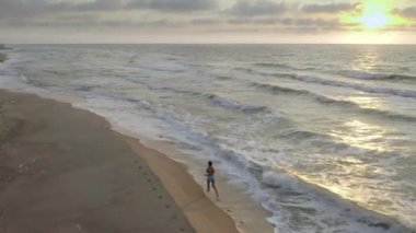 Gün batımında sahilde koşan bir kadın. Güzel bulutlar ve nefes kesici gün batımı.