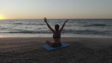 Güzel Genç Kadın Sahilde Gün Batımını izlerken Oturan Yoga Yapıyor.