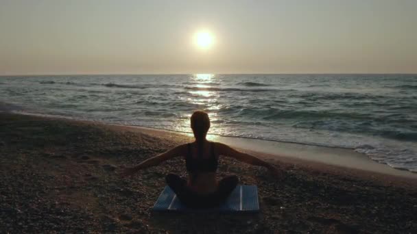 Hermosa joven haciendo yoga sentado en la playa mientras observa el atardecer . — Vídeos de Stock