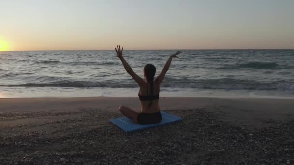 Hermosa joven haciendo yoga sentado en la playa mientras observa el atardecer . — Vídeos de Stock