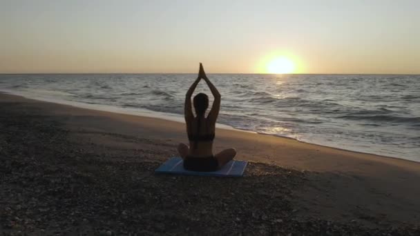 Όμορφη νεαρή γυναίκα κάνει καθιστή γιόγκα στην παραλία, ενώ βλέποντας το ηλιοβασίλεμα. — Αρχείο Βίντεο